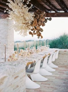 a long table with white chairs and flowers hanging from it's centerpieces