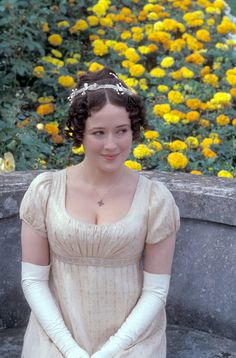 a woman in an old fashioned dress and white gloves standing next to a flower garden