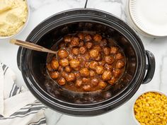 a crock pot filled with meatballs and corn next to other food on a table