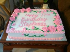 a birthday cake with pink roses on it sitting on top of a wooden table next to a candle