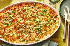 a large casserole dish with vegetables and meat in it next to silverware