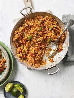 a pan filled with rice and limes next to two plates full of food on the table