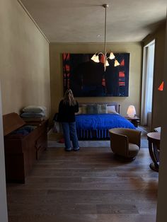 a woman standing in a bedroom next to a bed with blue bedspread on it