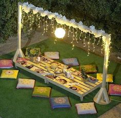 a table with pillows and lights on it in the middle of a lawn area at night