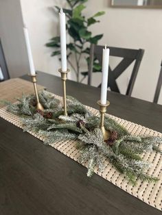 two candles are sitting on top of a placemat with pine cones and greenery