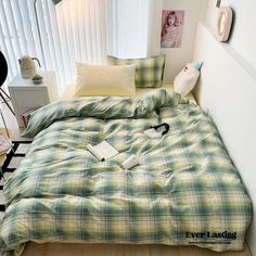 a bed with green and white plaid comforter next to a night stand on a hard wood floor