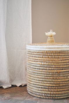 a large woven basket sitting on top of a stone floor next to a white curtain