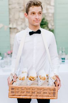 a young man holding a basket filled with food next to a table full of wine glasses