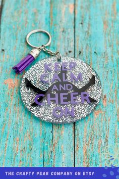 a purple and black keychain with the words keep calm and cheer on it