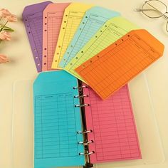 five colorful binders sitting on top of a table next to a pair of glasses