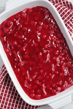 a white dish filled with cranberry sauce on top of a red and white checkered cloth