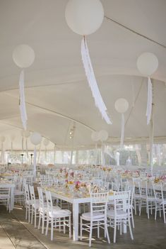 tables and chairs are set up in a tent with white balloons hanging from the ceiling