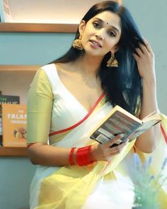 a woman in a yellow and white sari holding a book with her left hand