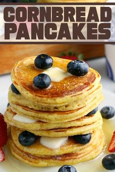 a stack of pancakes topped with blueberries and butter on a white plate next to strawberries