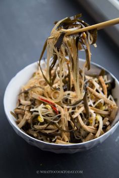 a bowl filled with noodles and chopsticks on top of a black table next to a window