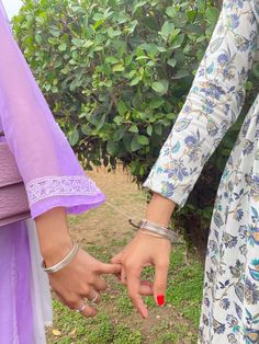 two women are holding hands in front of some bushes and trees with their fingers touching each other