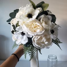 a person holding a bouquet of white flowers in their left hand, with greenery on the other side