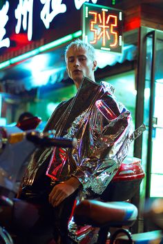 a man sitting on top of a motorcycle in front of a neon sign and building