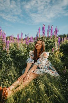 a woman sitting in the grass with purple flowers