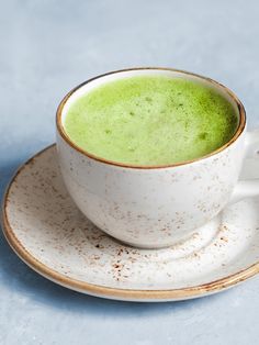 a white cup with green liquid in it on a saucer next to a spoon