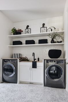 a washer and dryer in a small room with white shelves on the wall