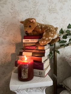 a teddy bear sitting on top of a stack of books next to a lit candle