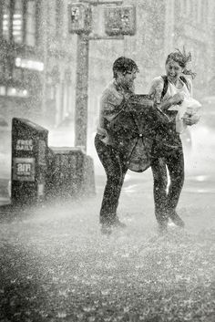 two people walking in the rain on a city street with an umbrella over their head