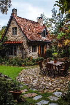 a stone house with a table and chairs in the front yard, surrounded by greenery