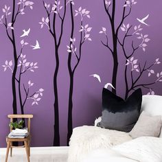 a purple wall with white trees and birds painted on the walls is next to a chair