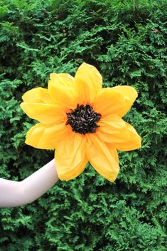 a large yellow flower on the end of a white pipe in front of some bushes