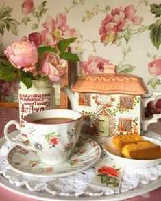 a tea cup and saucer on a table next to a plate with a piece of cake