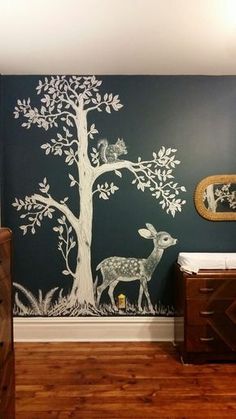 a baby's room with a tree painted on the wall next to a crib