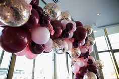 a bunch of balloons hanging from the ceiling in front of large windows with lots of shiny confetti