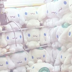 many white stuffed animals are stacked up in a store display case with blue eyes and mustaches on them