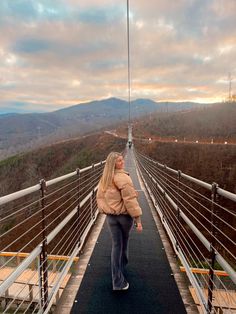 a woman is walking across a bridge with mountains in the backgrounds