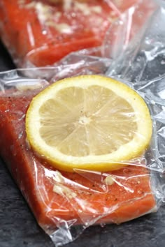 two pieces of salmon wrapped in plastic with a lemon