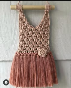 an orange and pink crocheted purse hanging from a wooden hanger on a white wall