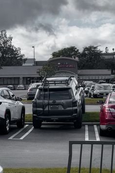 several cars are parked in a parking lot with cloudy skies behind them and the building is empty