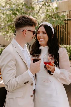 a man and woman standing next to each other holding wine glasses