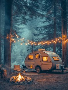 a camper parked in the woods next to a fire pit with lights strung over it