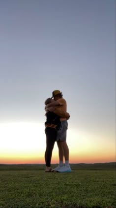 two people embracing each other in the middle of an open field at sunset or dawn