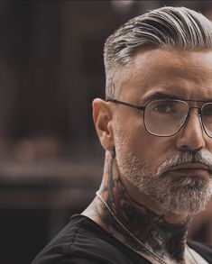 a man with grey hair and tattoos on his neck looking at the camera while wearing glasses