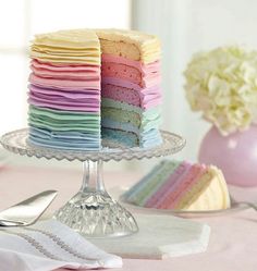 a multi - colored cake is on a glass plate with silverware and flowers in the background