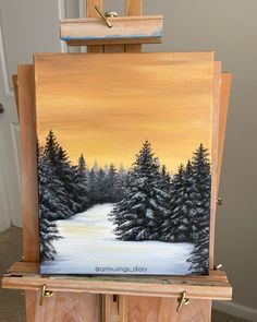 an easel with a painting on it that has snow covered trees in the background