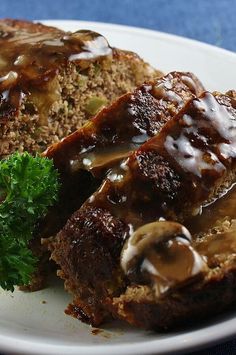 meatloaf with mushrooms and gravy on a white plate next to parsley