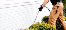 a man in brown pants and black shirt using a pressure washer on the side of a house