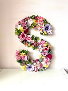 the letter s is made up of flowers and greenery on top of a white surface