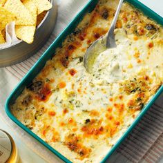 a casserole dish with cheese and spinach in it next to some tortilla chips