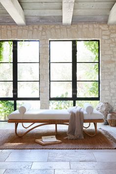 a room with two windows and a bench in the middle, near an area rug