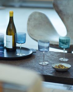 three wine glasses sitting on top of a wooden table next to a bottle of wine